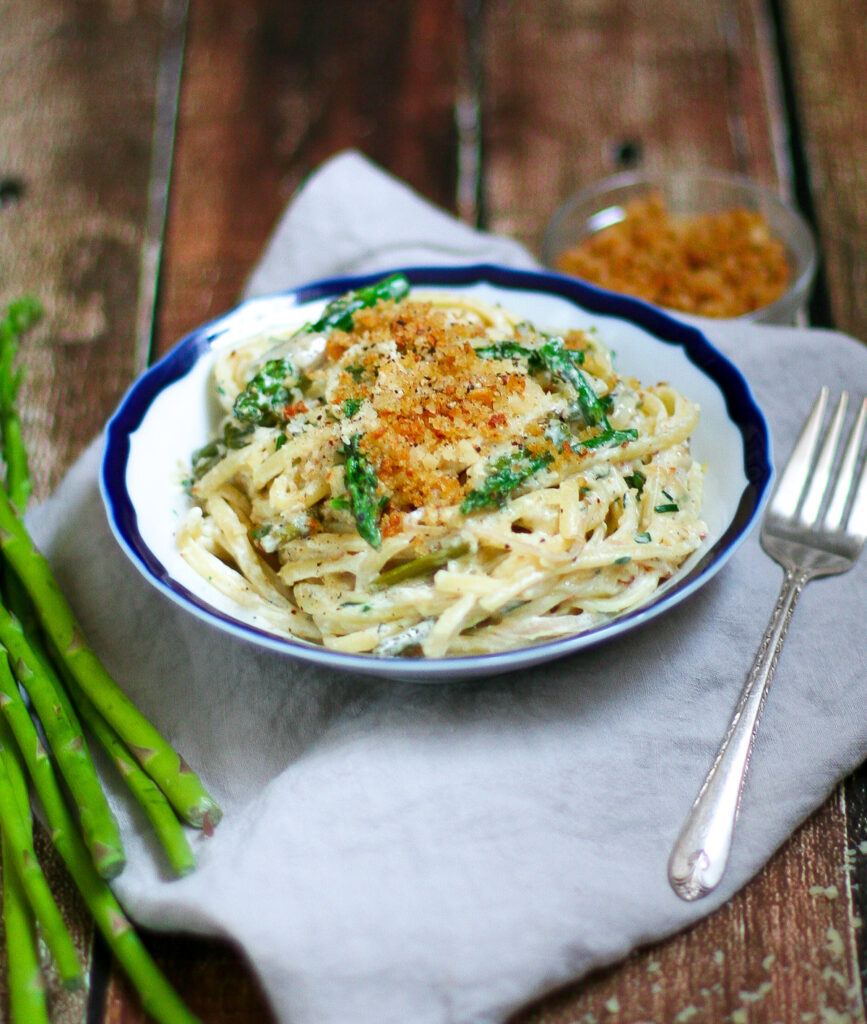 Side view of fettuccine pasta with asparagus, creme fraiche sauce, and golden breadcrumbs